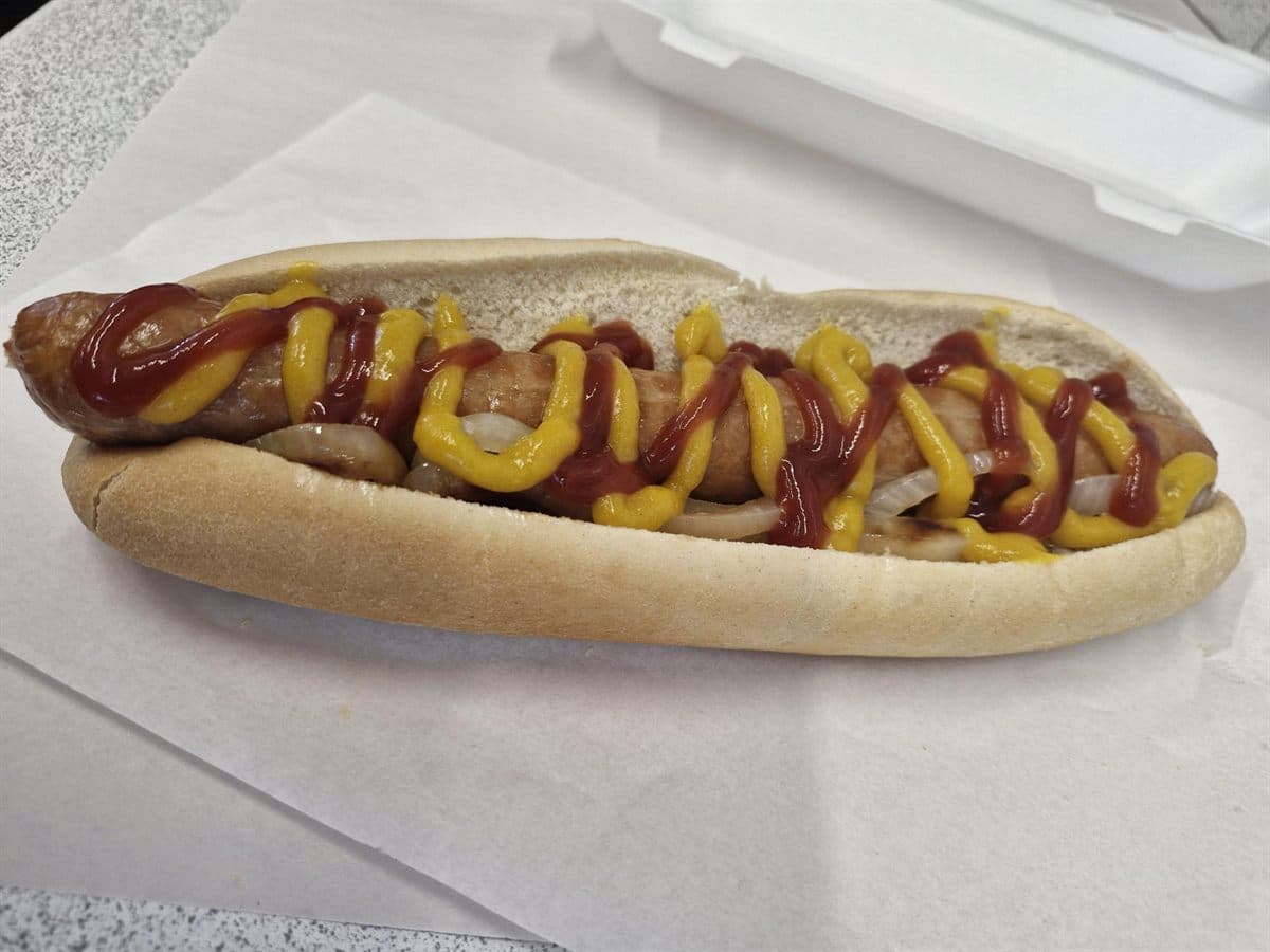 A Bigfoot hotdog in a long bun, topped with onions and zigzags of ketchup and mustard