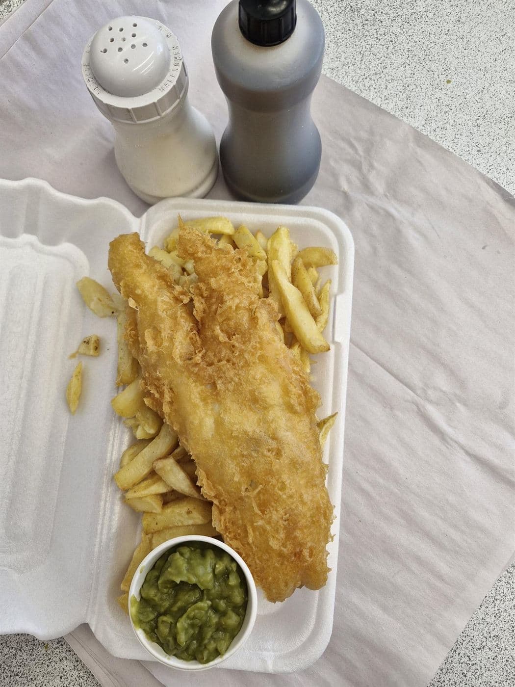 Battered fish on a bed of chips with a pot of mushy peas from The Goldfish Bowl